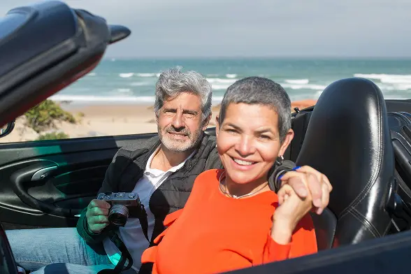 happy retired couple sitting in car by beach from financial security