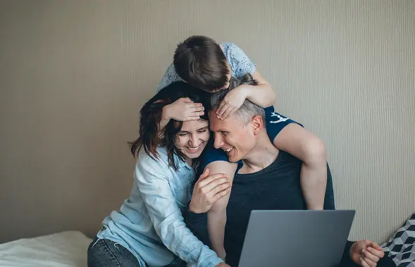 family happy with health insurance quotes mom, father, and kid hugging in bed with computer
