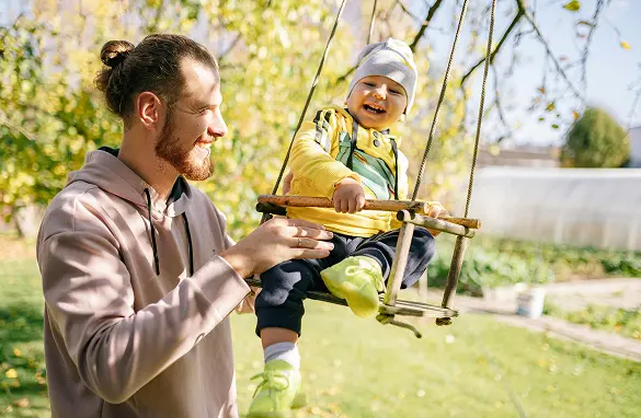 young dad pushing his baby in a swing happy with financial security